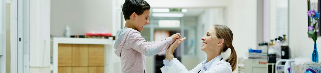 Un médecin souriant joue avec un jeune patient dans un cadre médical lumineux et accueillant, illustrant l'importance des soins attentionnés. Cette image reflète le soutien apporté par l'application FYWY aux personnes souffrant de maladies inflammatoires chroniques de l'intestin (MICI), telles que la rectocolite hémorragique et la maladie de Crohn, en facilitant la gestion des symptômes et en offrant des conseils médicaux adaptés.